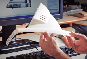 a white 3d printed part being examined next to a computer monitor