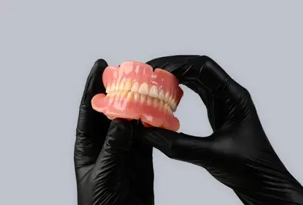 Black gloved hands holding Stratasys TrueDent Dentures